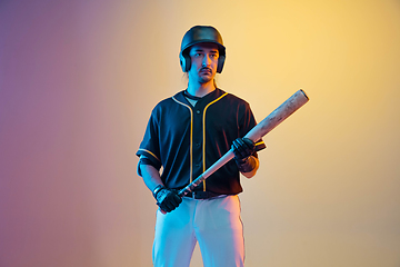 Image showing Baseball player, pitcher in a black uniform practicing on gradient background in neon light