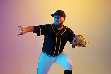 Image showing Baseball player, pitcher in a black uniform practicing on gradient background in neon light