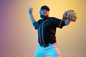 Image showing Baseball player, pitcher in a black uniform practicing on gradient background in neon light