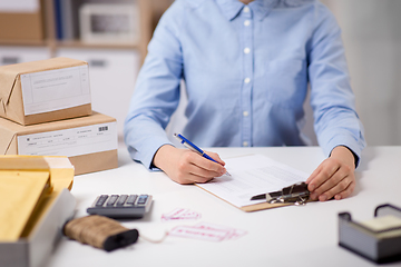 Image showing woman with clipboard and parcels at post office