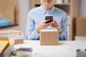 Image showing woman with smartphone and parcels at post office