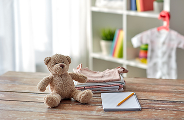 Image showing baby clothes, teddy bear toy and notebook