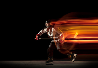 Image showing Young female hockey player with the stick on black background in neon light