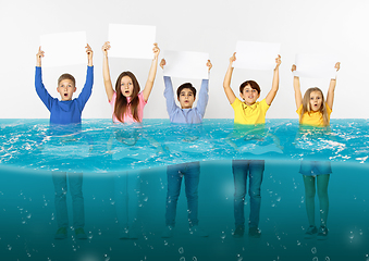 Image showing Group of children with blank white banners standing in water of melting glacier, global warming