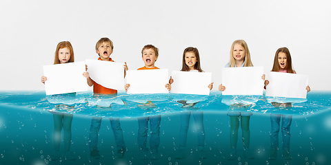 Image showing Group of children with blank white banners standing in water of melting glacier, global warming