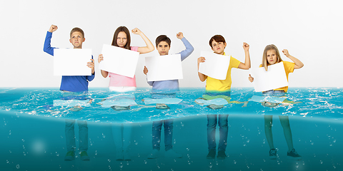 Image showing Group of children with blank white banners standing in water of melting glacier, global warming