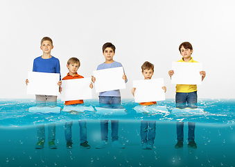 Image showing Group of children with blank white banners standing in water of melting glacier, global warming