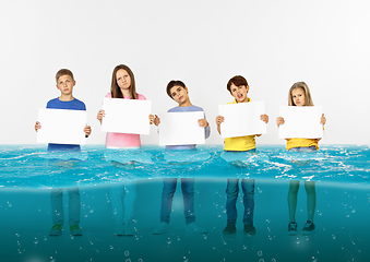 Image showing Group of children with blank white banners standing in water of melting glacier, global warming