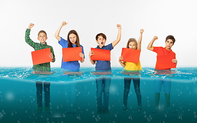 Image showing Group of children with blank red banners standing in water of melting glacier, global warming