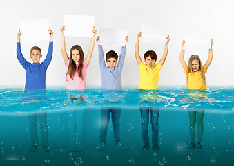 Image showing Group of children with blank white banners standing in water of melting glacier, global warming