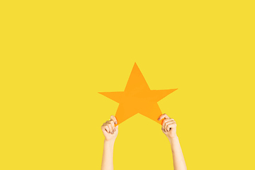 Image showing Hands holding the sign of star on yellow studio background