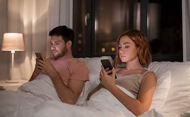 Image showing couple using smartphones in bed at night at home
