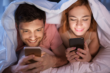 Image showing happy couple using smartphones in bed at night