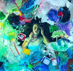 Image showing Woman drowning in ocean water under plastic recipients pile, environment concept