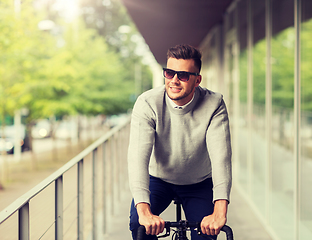 Image showing young man in shades riding bicycle on city street