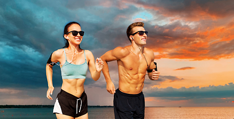 Image showing couple with phones and arm bands running over sea