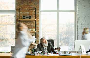 Image showing Tired boss resting at his workplace while people moving near blurred