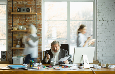 Image showing Nervous and tired boss at his workplace busy while people moving near blurred