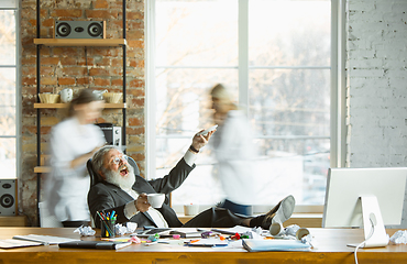 Image showing Tired boss resting at his workplace while people moving near blurred