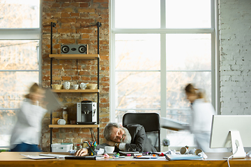 Image showing Tired boss resting at his workplace while people moving near blurred