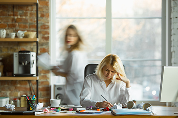 Image showing Nervous and tired boss at her workplace busy while people moving near blurred