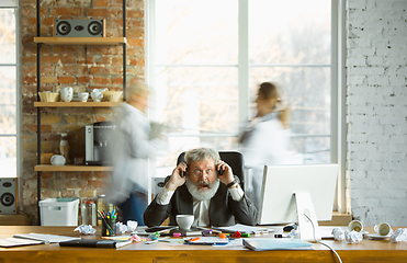 Image showing Nervous and tired boss at his workplace busy while people moving near blurred