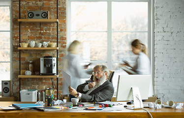 Image showing Nervous and tired boss at his workplace busy while people moving near blurred