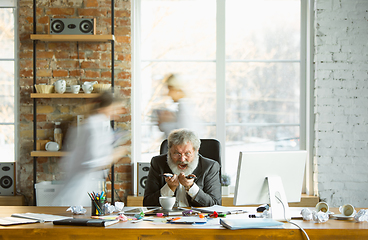 Image showing Nervous and tired boss at his workplace busy while people moving near blurred