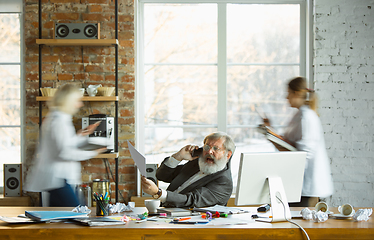 Image showing Nervous and tired boss at his workplace busy while people moving near blurred