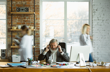 Image showing Nervous and tired boss at his workplace busy while people moving near blurred