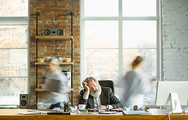 Image showing Nervous and tired boss at his workplace busy while people moving near blurred