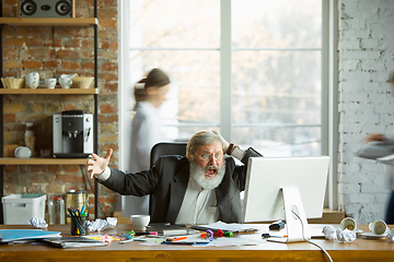 Image showing Nervous and tired boss at his workplace busy while people moving near blurred