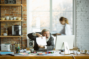 Image showing Nervous and tired boss at his workplace busy while people moving near blurred