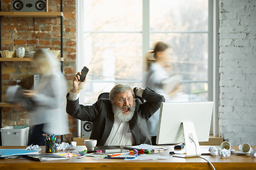 Image showing Nervous and tired boss at his workplace busy while people moving near blurred