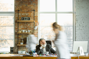 Image showing Tired boss resting at his workplace while people moving near blurred