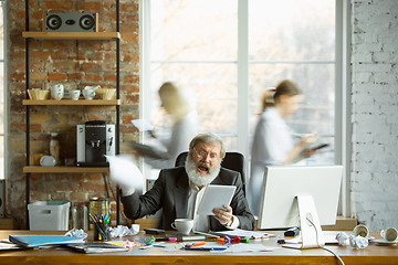 Image showing Nervous and tired boss at his workplace busy while people moving near blurred