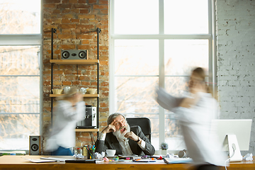 Image showing Tired boss resting at his workplace while people moving near blurred