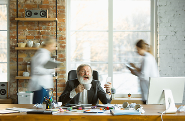 Image showing Tired boss resting at his workplace while people moving near blurred
