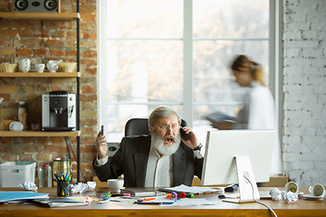 Image showing Nervous and tired boss at his workplace busy while people moving near blurred