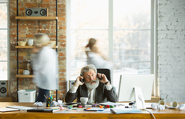 Image showing Nervous and tired boss at his workplace busy while people moving near blurred