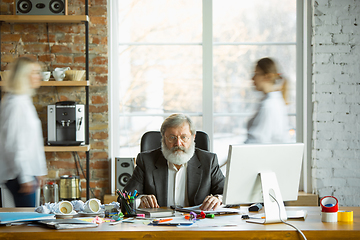 Image showing Nervous and tired boss at his workplace busy while people moving near blurred