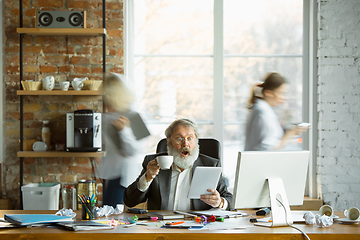 Image showing Nervous and tired boss at his workplace busy while people moving near blurred