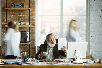 Image showing Nervous and tired boss at his workplace busy while people moving near blurred