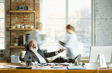 Image showing Tired boss resting at his workplace while people moving near blurred