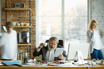 Image showing Nervous and tired boss at his workplace busy while people moving near blurred