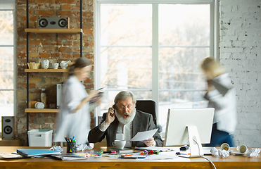 Image showing Nervous and tired boss at his workplace busy while people moving near blurred