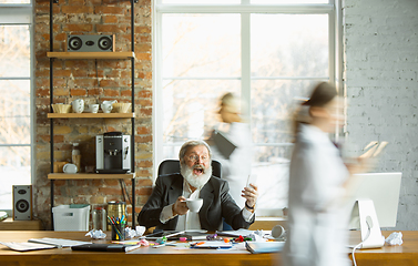 Image showing Tired boss resting at his workplace while people moving near blurred