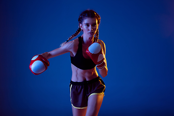 Image showing Fit caucasian woman in sportswear boxing on blue studio background in neon light