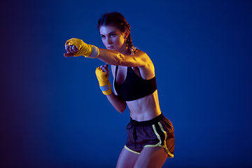 Image showing Fit caucasian woman in sportswear boxing on blue studio background in neon light