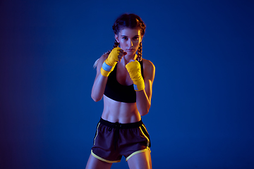 Image showing Fit caucasian woman in sportswear boxing on blue studio background in neon light